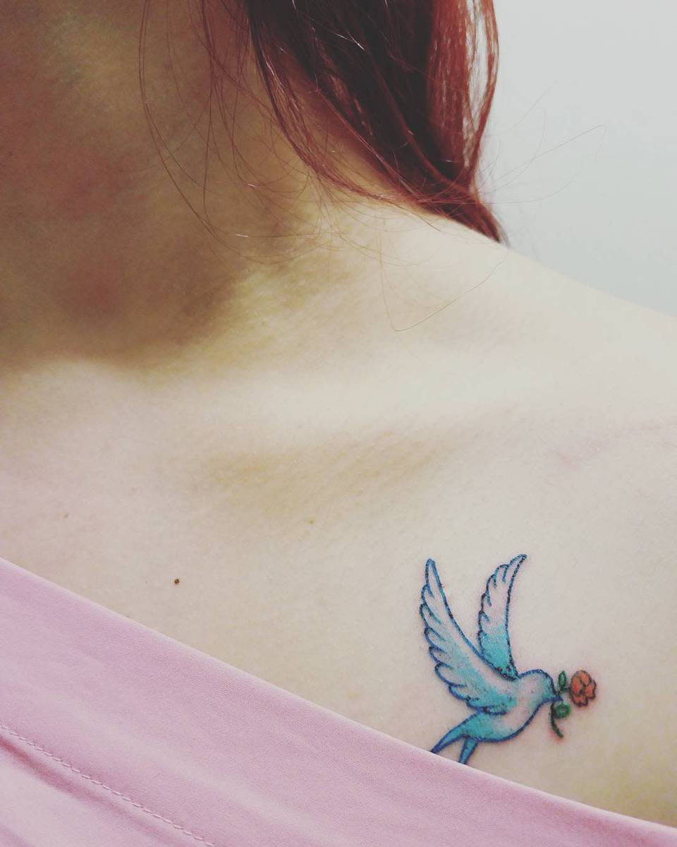 Shoulder tattoo of a blue bird holding a red flower in its beak, with wearer in pink garment