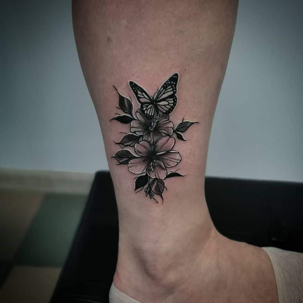 A delicate tattoo of a butterfly gracefully rests among vibrant flowers on a person's leg