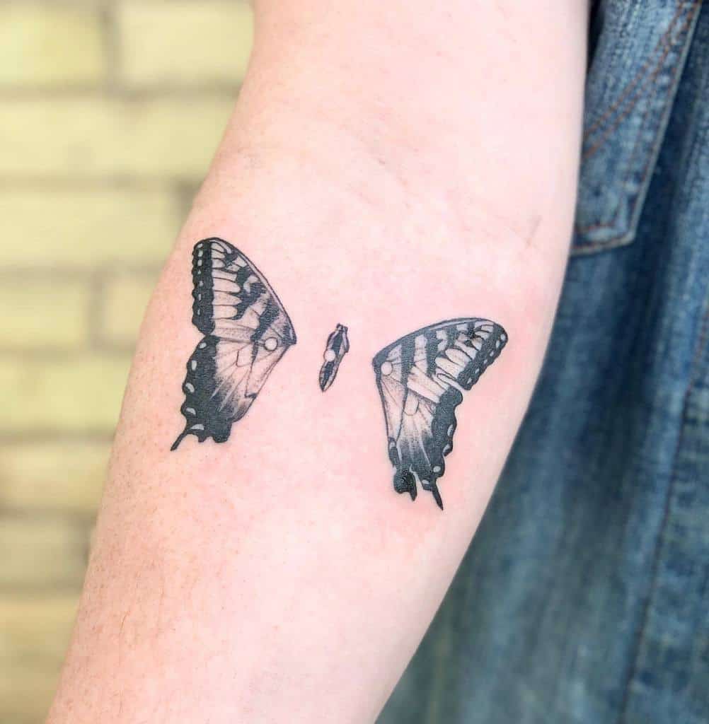 A delicate butterfly wings tattoo graces the forearm, framing a small silhouette elegantly nestled between them