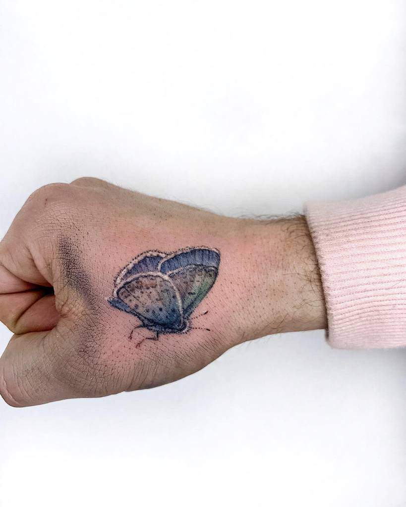 Realistic blue butterfly tattoo on the back of the hand, showcasing soft gradients and delicate detailing for a natural look