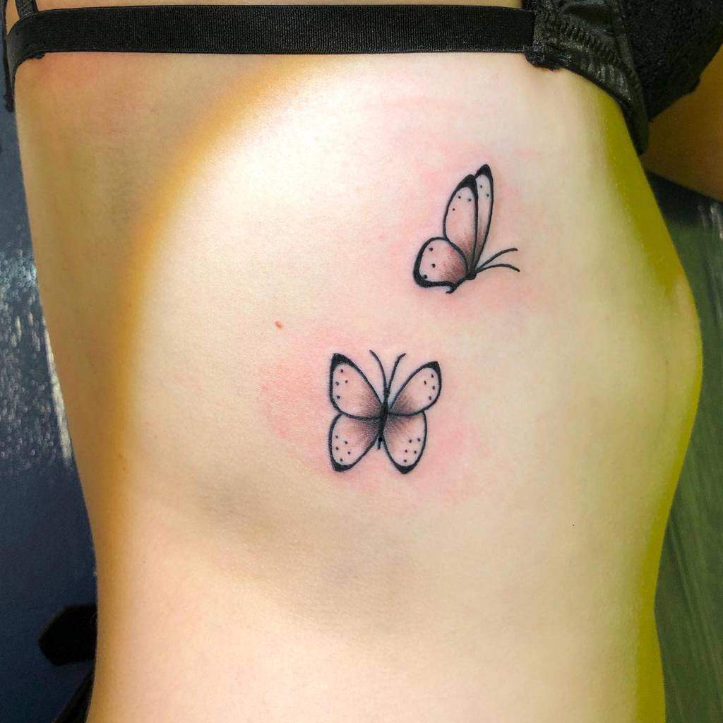 Two delicate butterfly tattoos on the ribcage, featuring soft shading and minimalist black ink for a graceful design