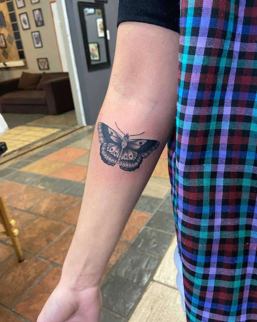 Detailed black and gray butterfly tattoo on the inner forearm, featuring intricate shading and realistic wing patterns.