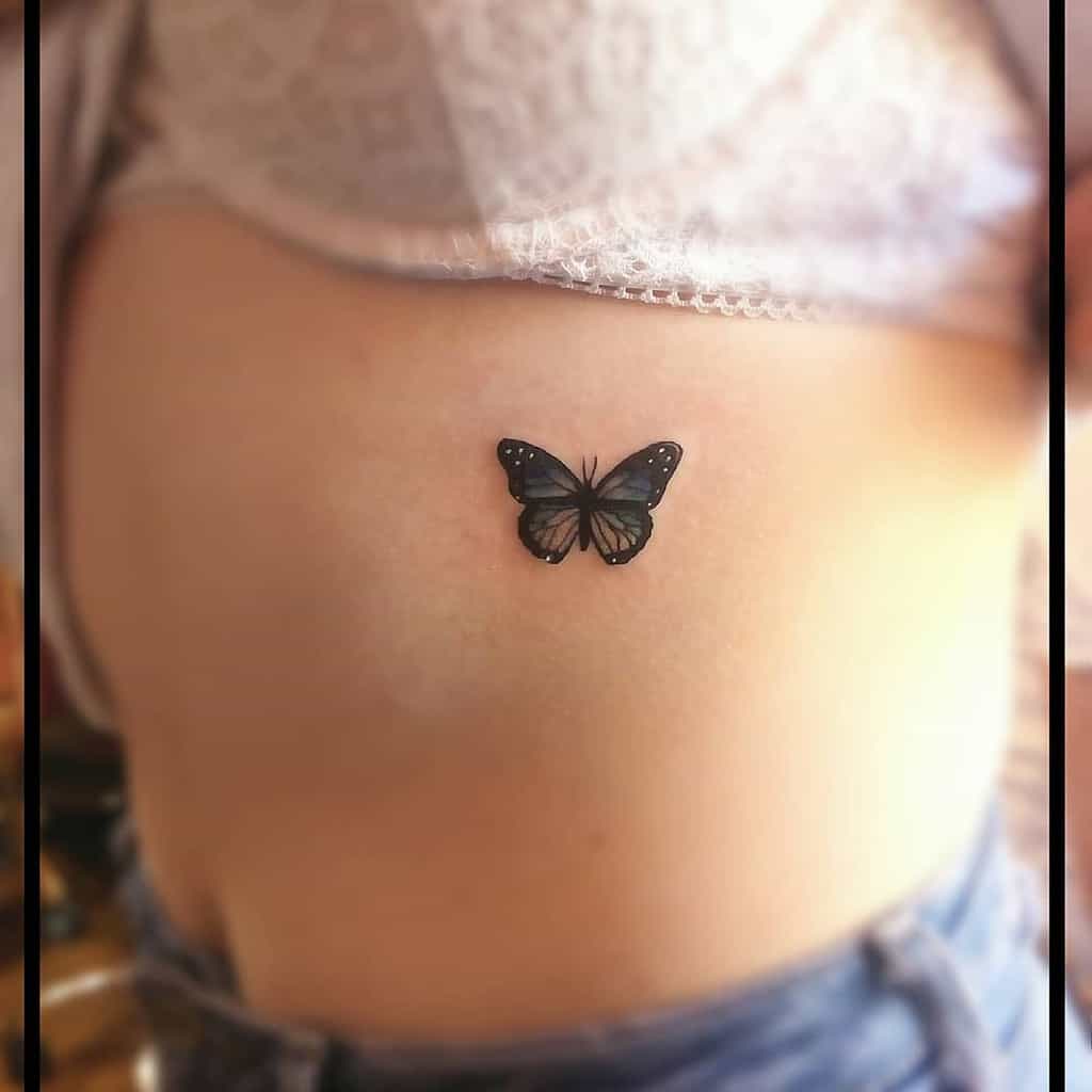 Small black butterfly tattoo on the side of the torso, with delicate details and soft shading for an elegant, subtle look.