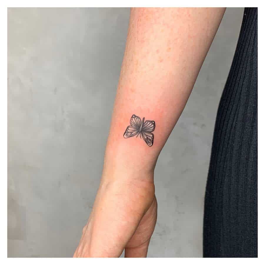Minimalist black and gray butterfly tattoo on the wrist, featuring fine lines and soft shading for a delicate, elegant look.