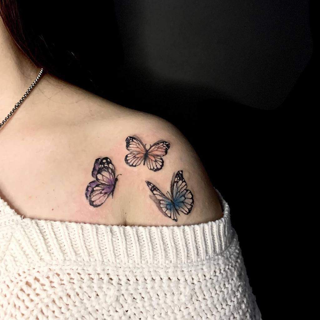 Three delicate butterfly tattoos on the shoulder, featuring soft pastel colors and fine details for a dreamy, elegant look.