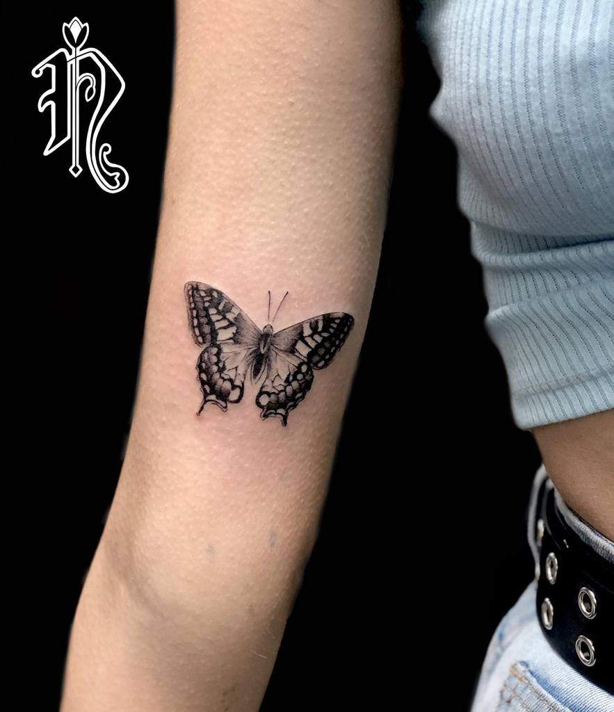 Realistic black and gray butterfly tattoo on the forearm, with intricate shading and fine details for a bold yet elegant look.