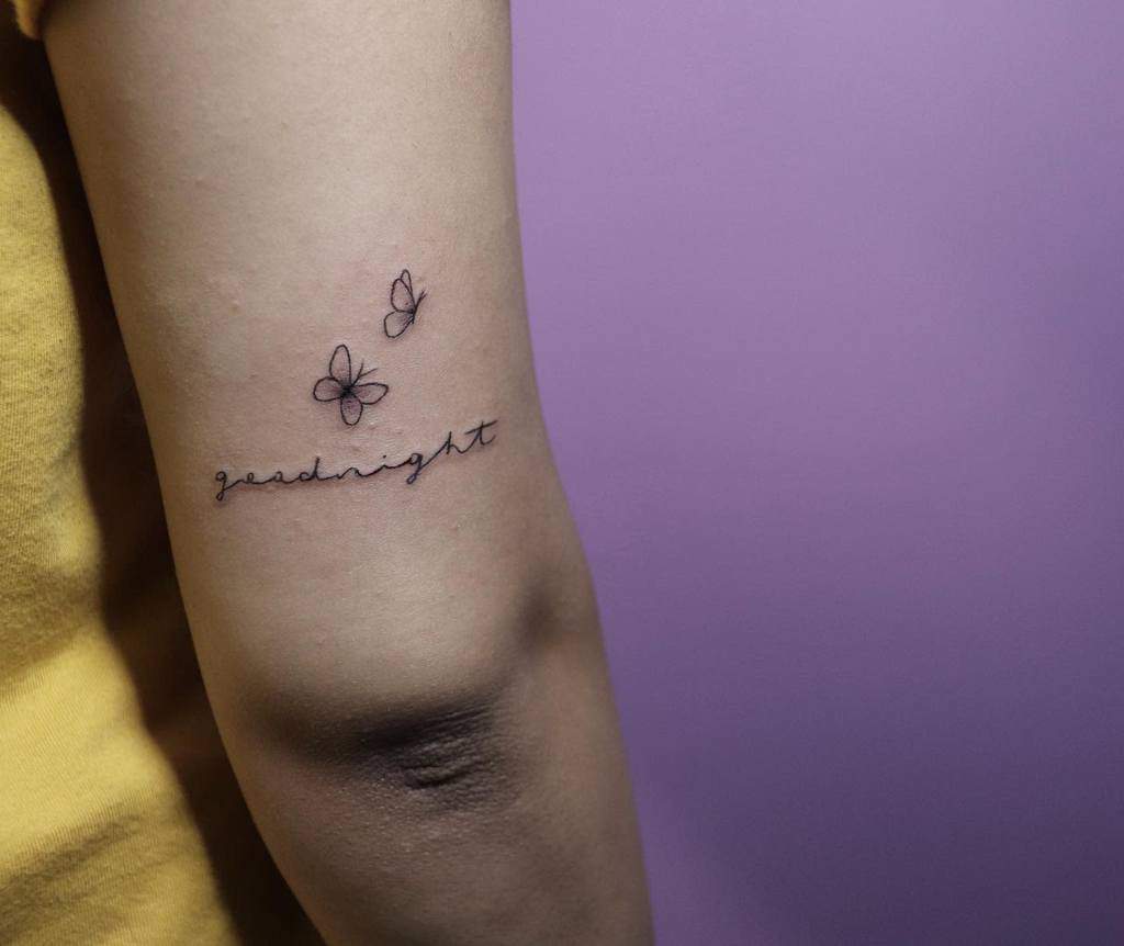 Minimalist butterfly tattoo with the word 'goodnight' in cursive on the arm, featuring delicate line art for an elegant touch.
