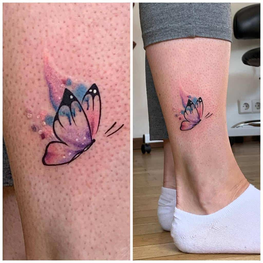Watercolor butterfly tattoo on the lower leg, featuring soft pink and blue hues with delicate black outlines for a dreamy effect.