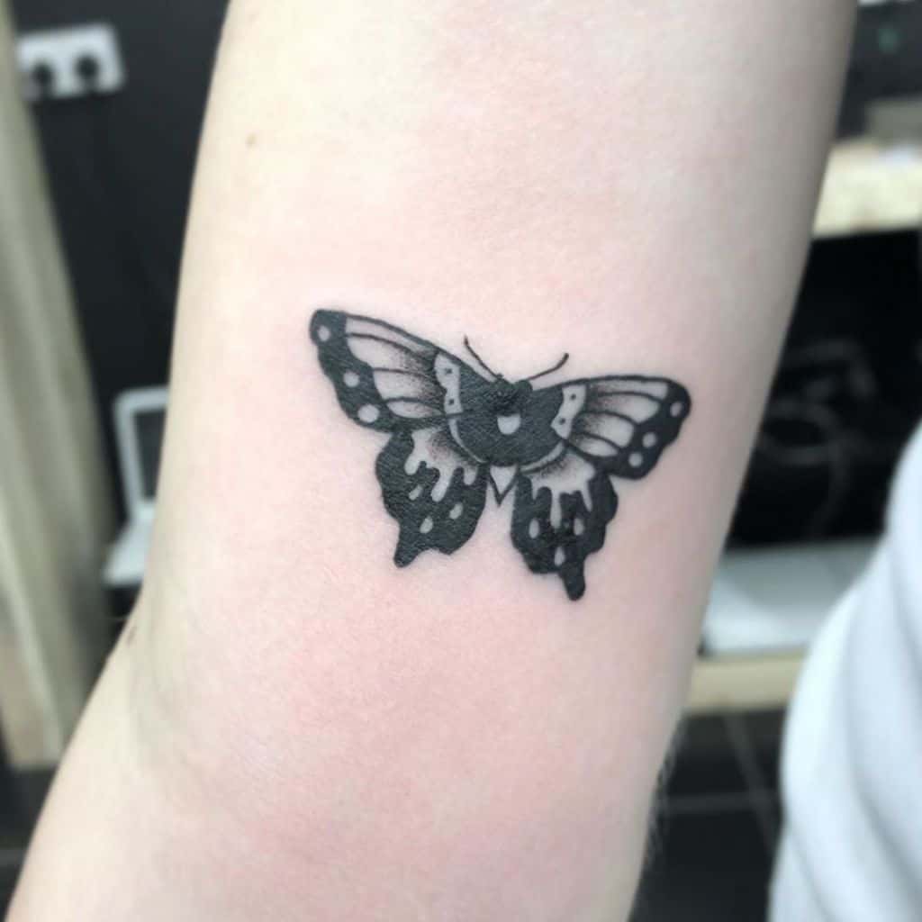 A striking tattoo on the forearm features a black and gray butterfly