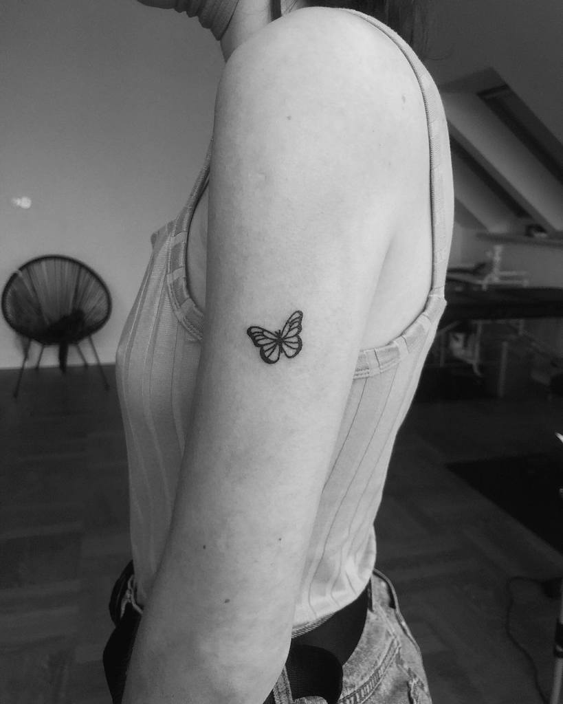 Small butterfly tattoo on the upper arm, featuring clean black linework for a minimalist and elegant design