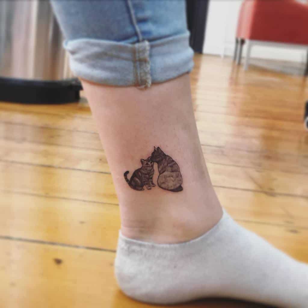 Ankle tattoo of two cats sitting together, one nuzzling the other