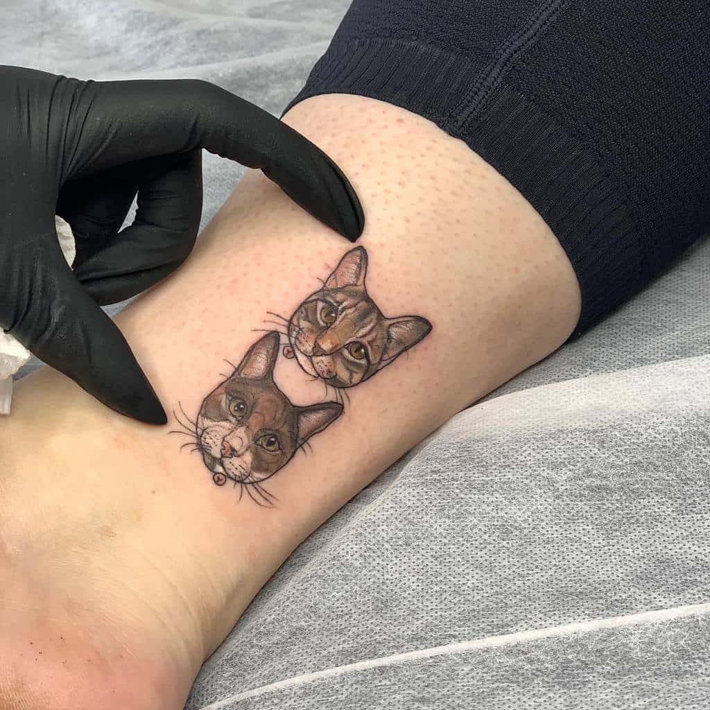 Ankle tattoo featuring two realistic cat portraits stacked vertically, detailed with vibrant colors and shading