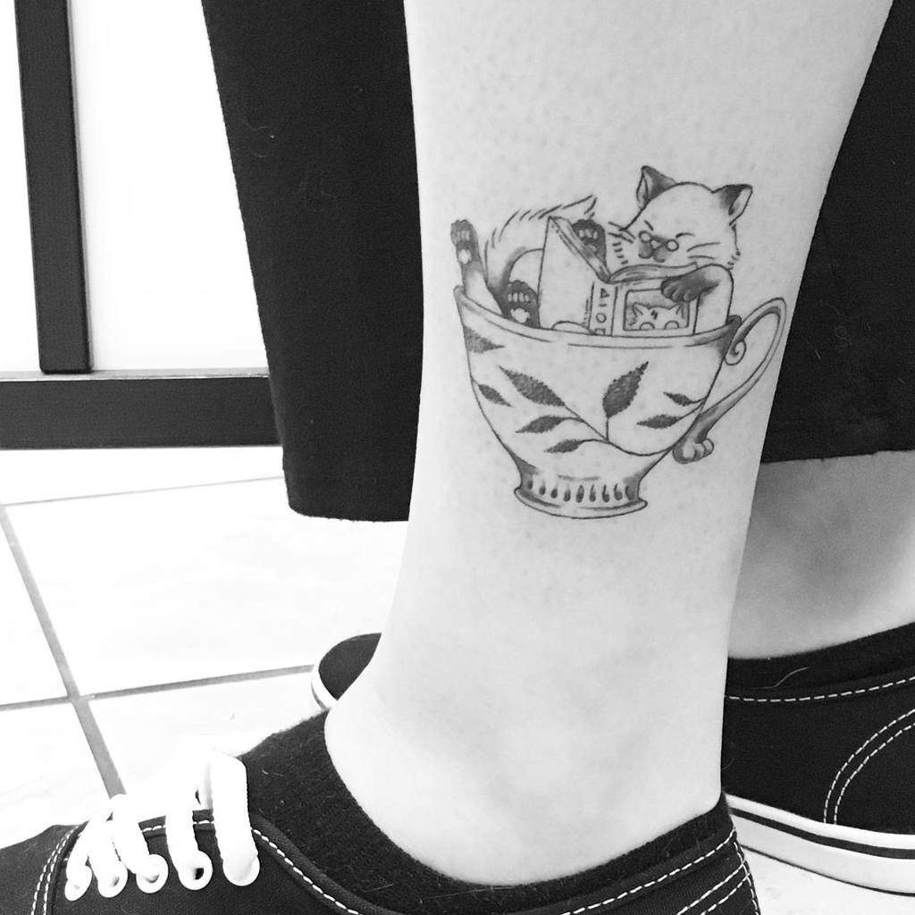 Tattoo of a cat in a teacup on a person's ankle