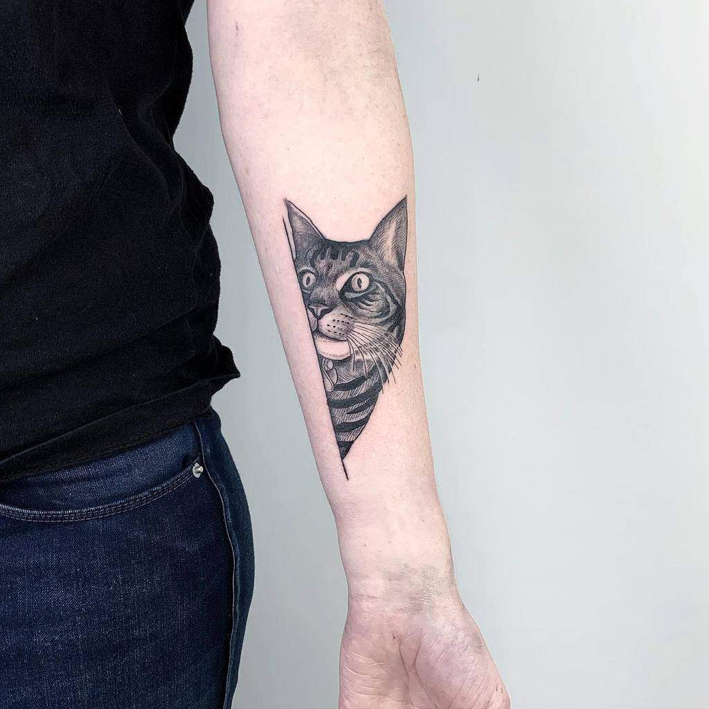 Forearm tattoo of a cat's head with wide eyes and tongue out