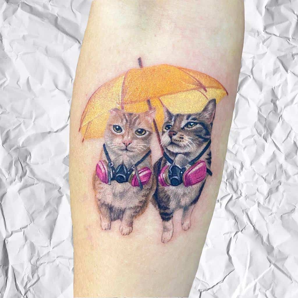 Tattoo of two cats with backpacks under a yellow umbrella