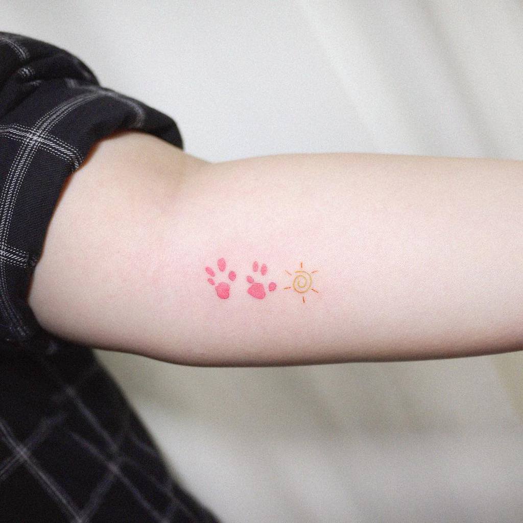 Arm with two pink cat paw print tattoos and a small orange sun tattoo