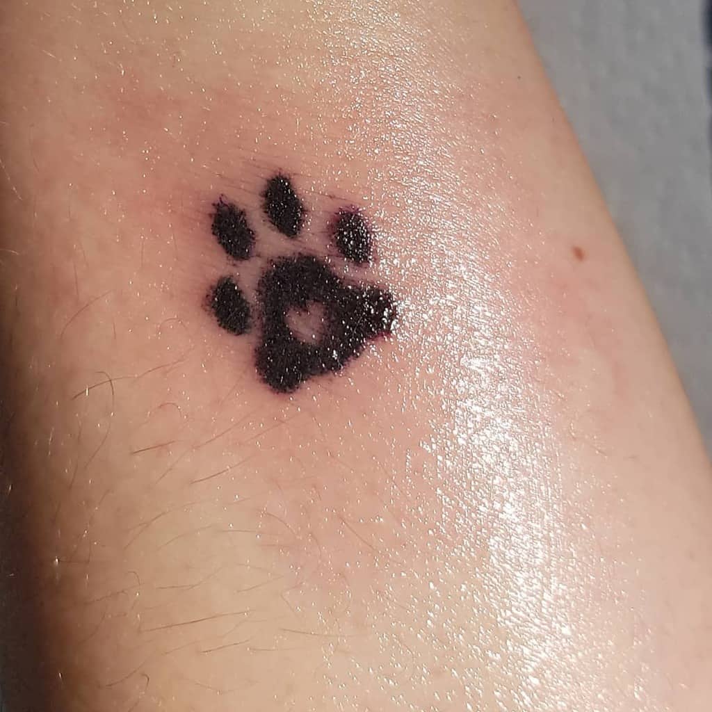 Small black cat paw print tattoo on light skin