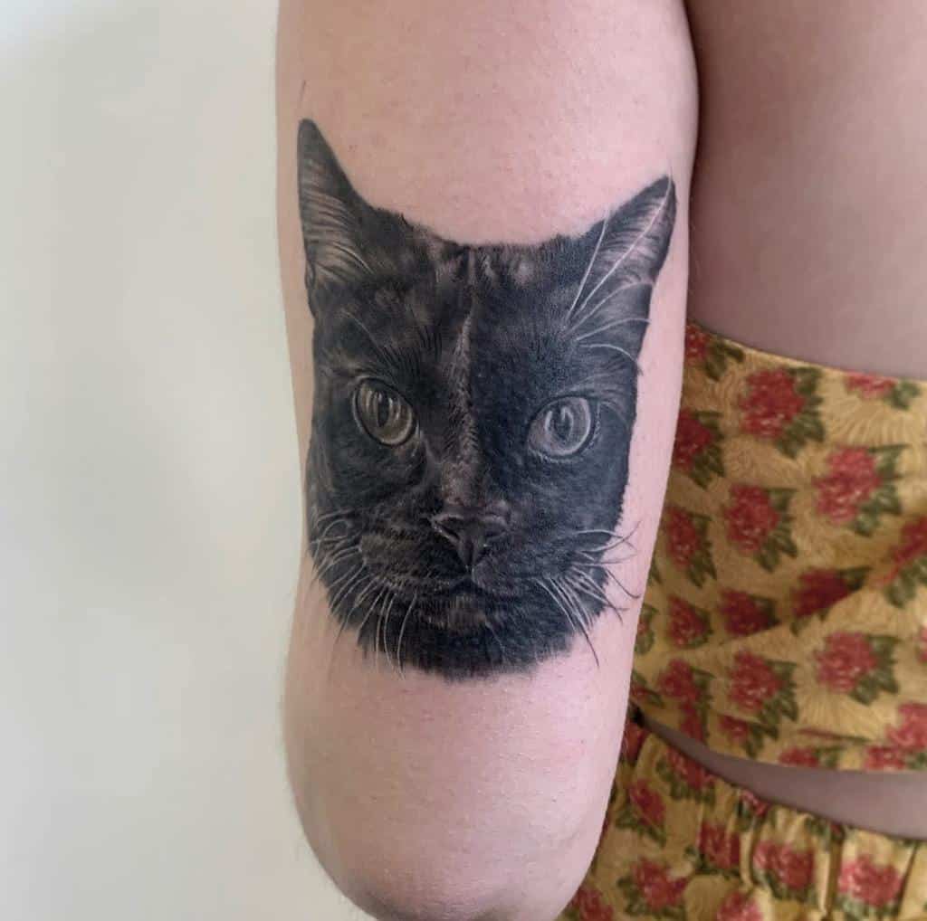 A realistic black cat tattoo on a person's upper arm