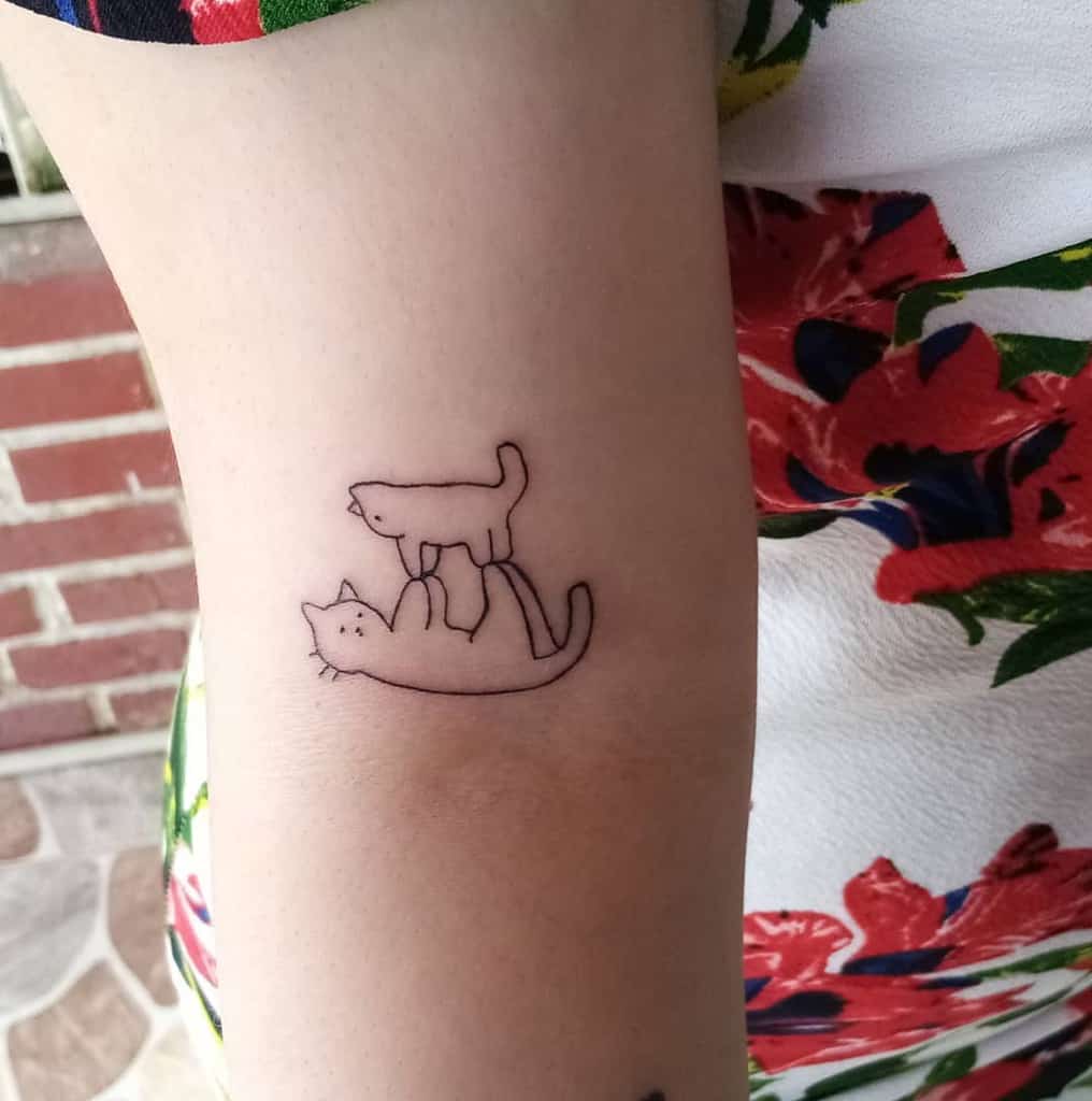 Simple tattoo of two outline cats on an arm 