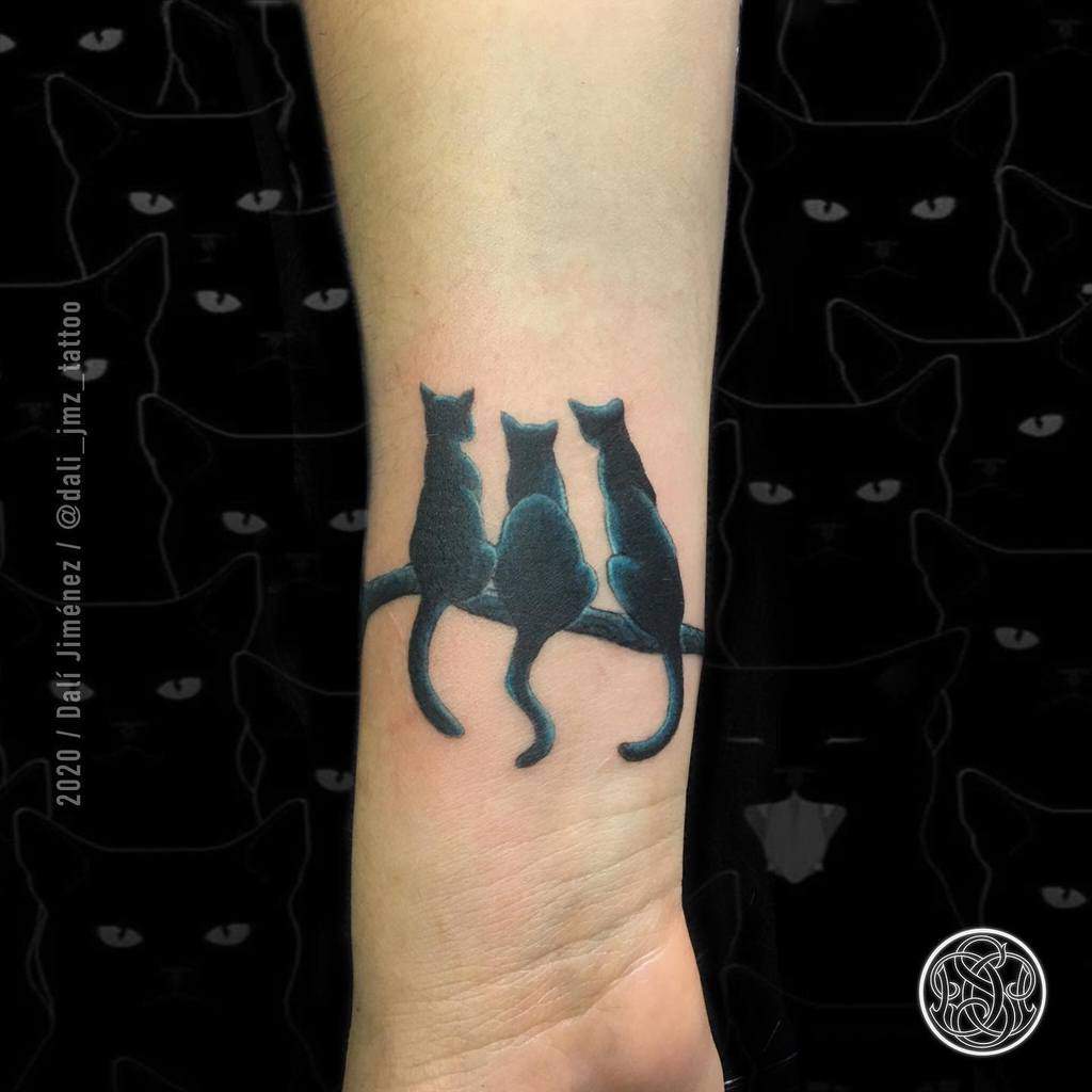 Tattoo of three black cats sitting together on a forearm