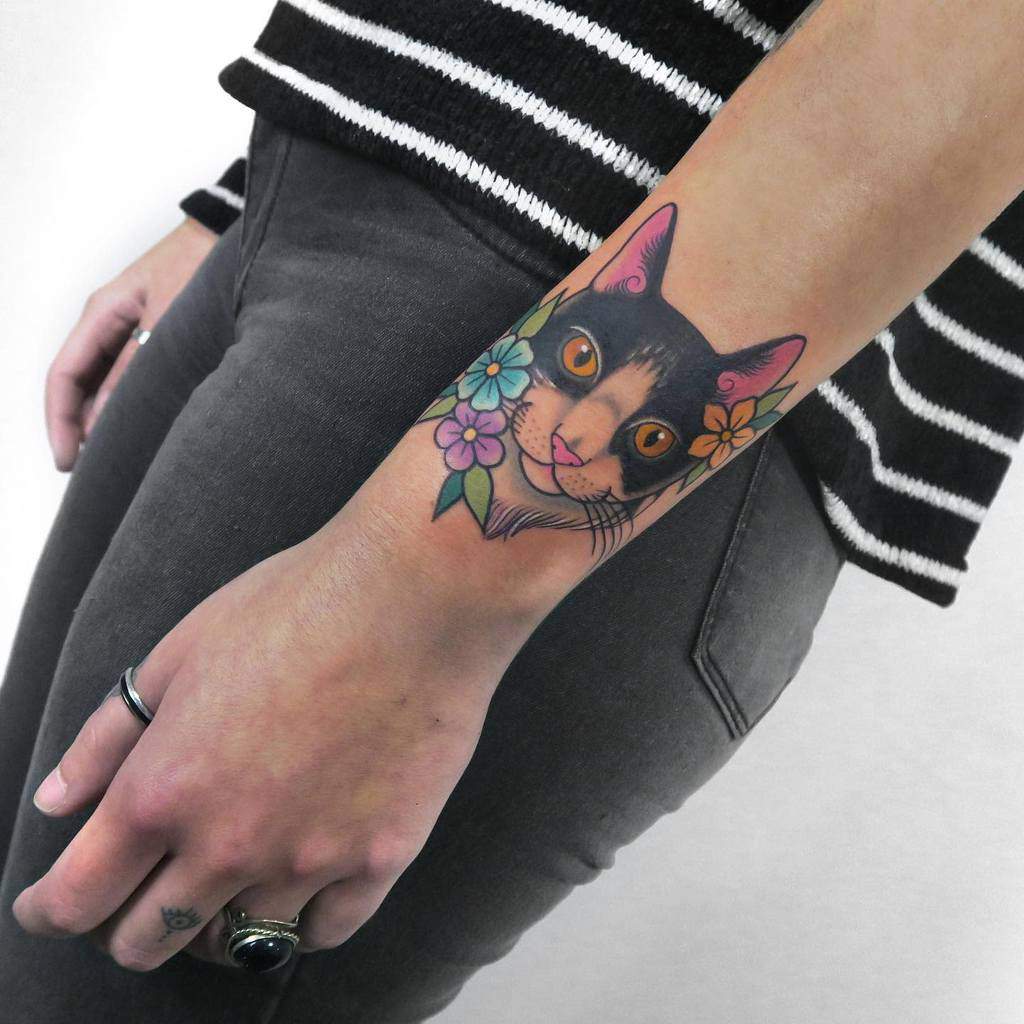 Colorful cat tattoo on a wrist with flowers around it