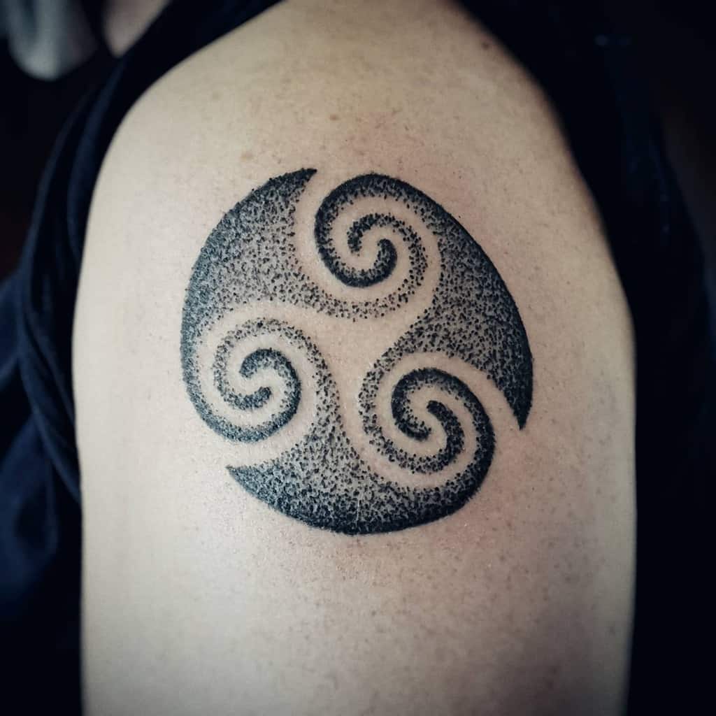 Close-up of a black triskelion tattoo with a dotwork style on an upper arm