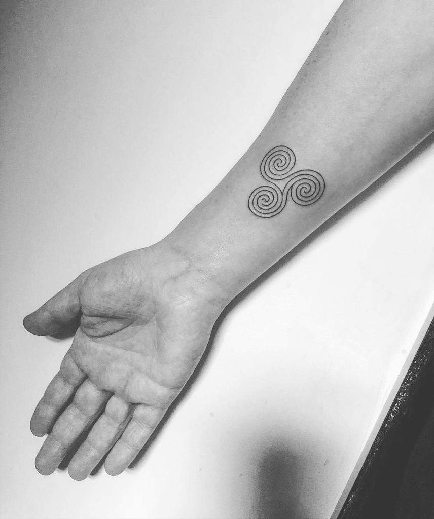 A forearm with a spiral triskelion tattoo near the wrist