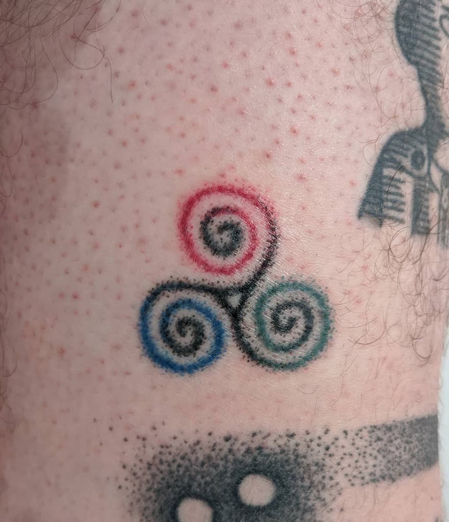 A triskelion tattoo with red, blue, and green spirals