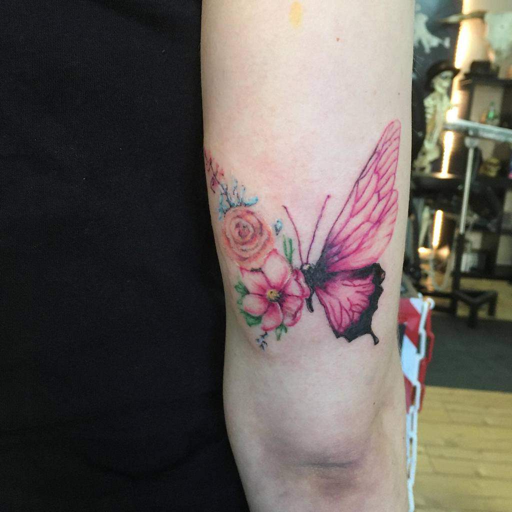 Pink butterfly tattoo paired with colorful floral designs, blending soft petals and intricate wing details on the arm