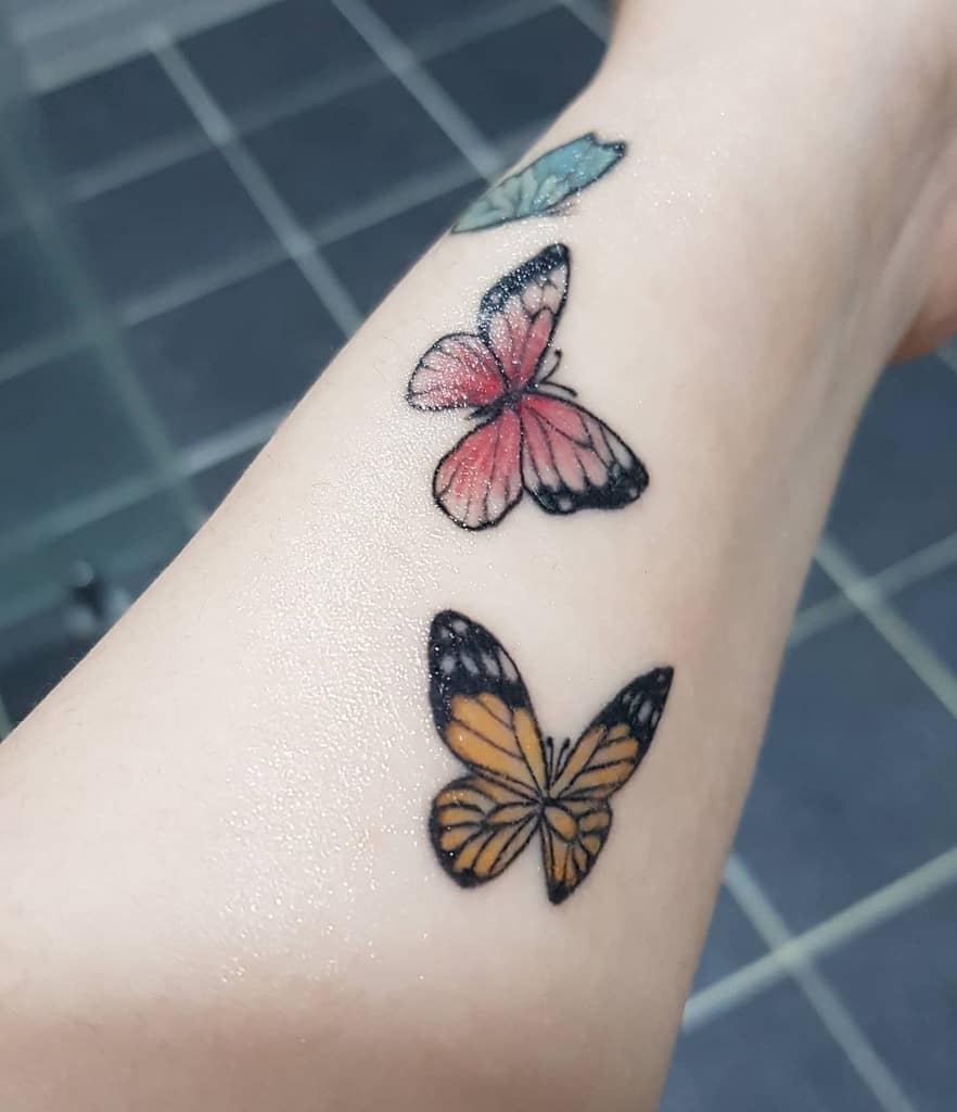 A vibrant trio of butterfly tattoos gracefully adorns the person's arm, each showcasing a spectrum of colors