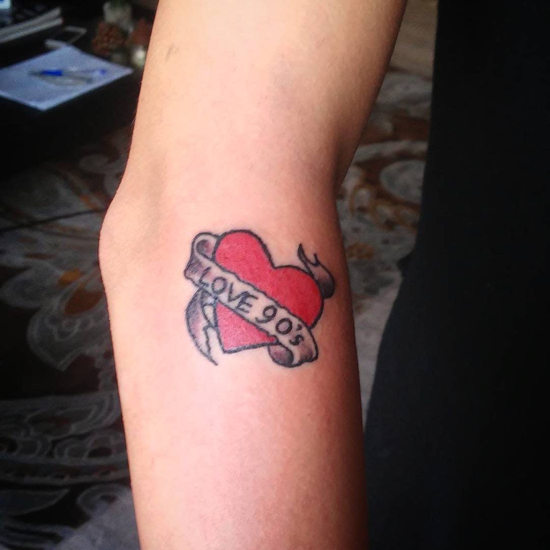 Tattoo of a red heart with a banner reading "LOVE 905" on an arm