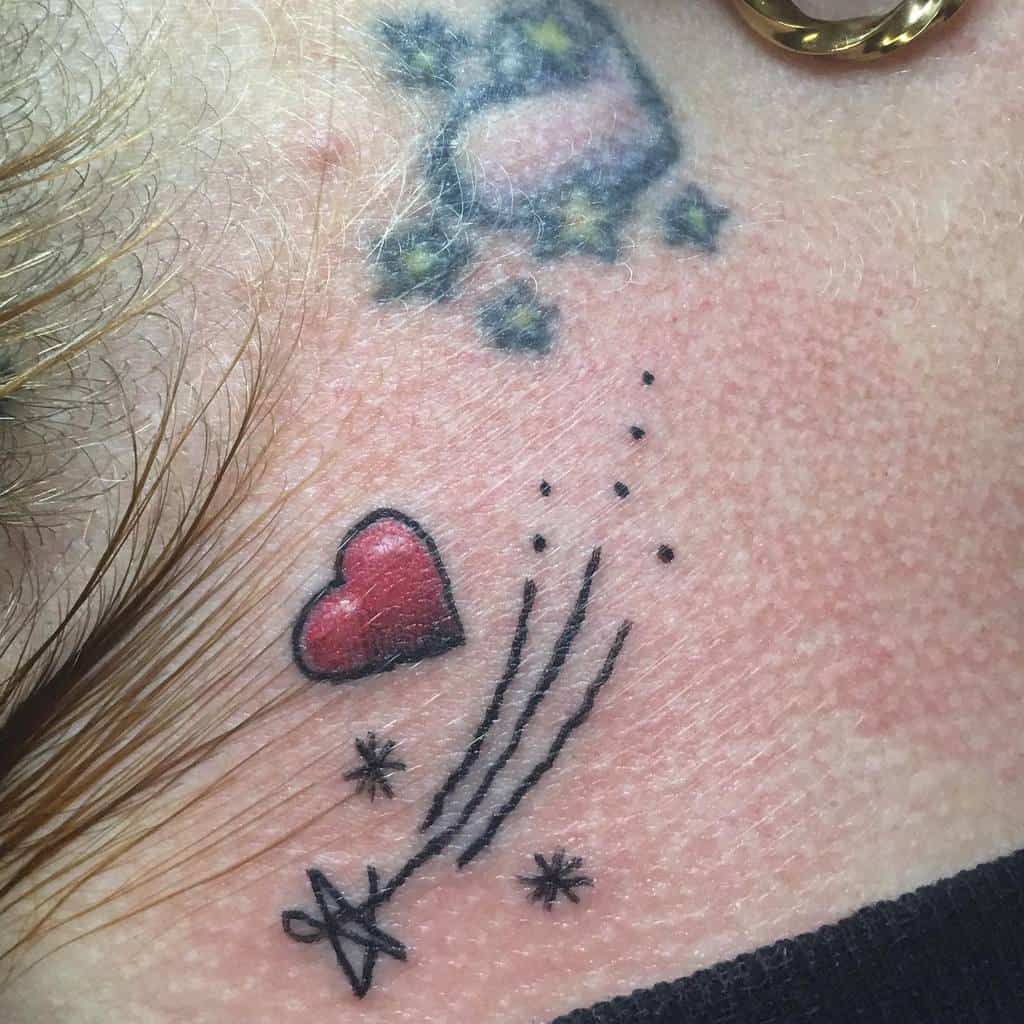 Tattoo of a red heart with trailing lines and black stars, located on the skin near the neck area