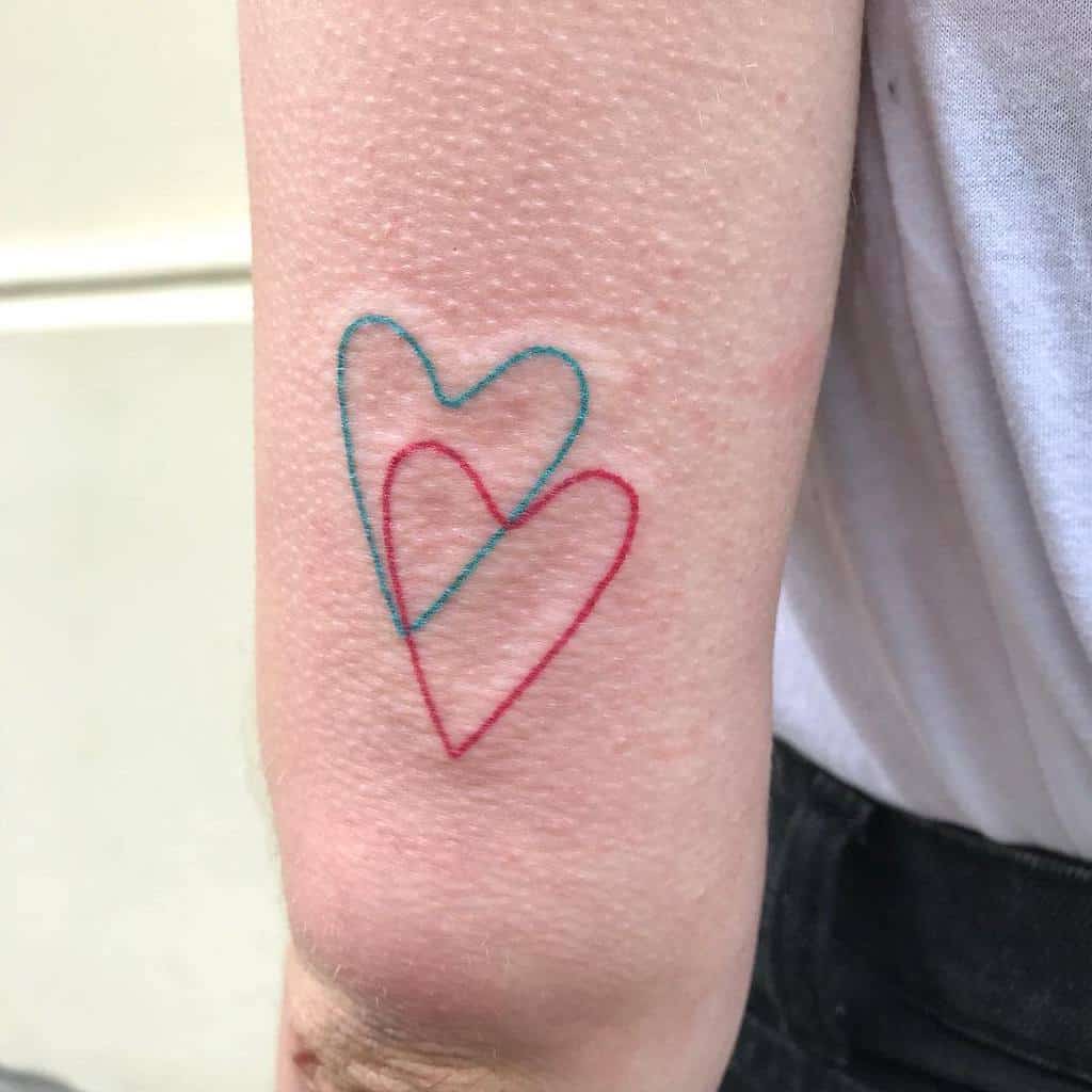 Minimalist tattoo of two overlapping hearts, one in blue and one in red, on a forearm