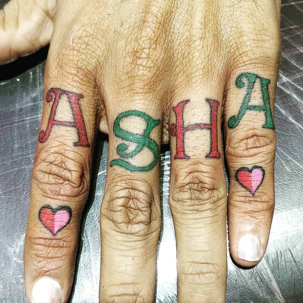 Fingers with tattoos spelling "ASHA" and small hearts on either side of the word