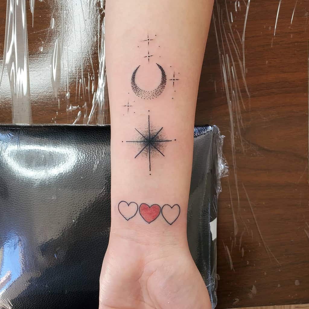 Arm tattoo with a crescent moon, star, and three hearts, with one heart filled in red