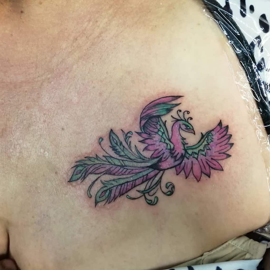 A small tattoo of a phoenix with striking green and pink wings on the upper chest