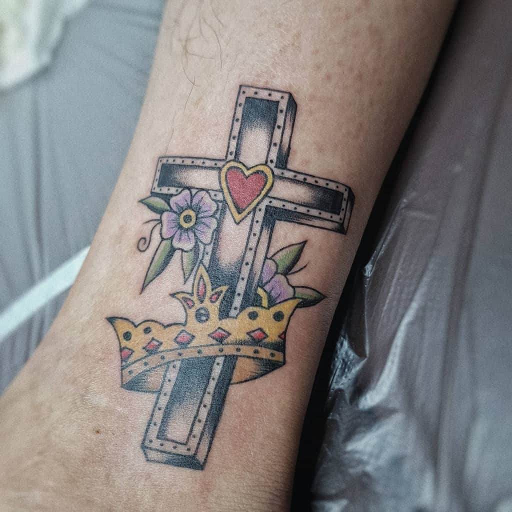 Tattoo of a decorated cross with flowers, heart, and a crown on a person's skin