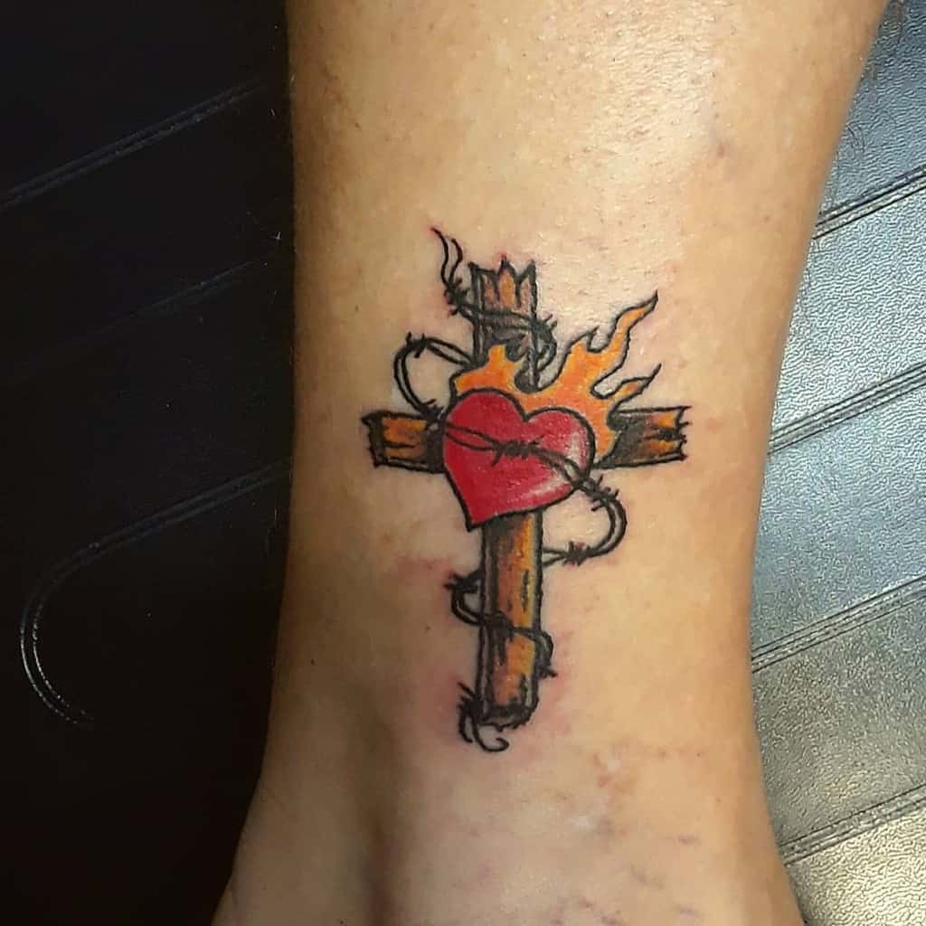 Tattoo of a cross with a heart, wrapped in thorns and topped with flames