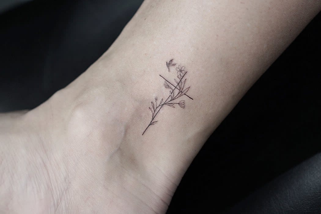 A delicate floral tattoo with a cross on an ankle