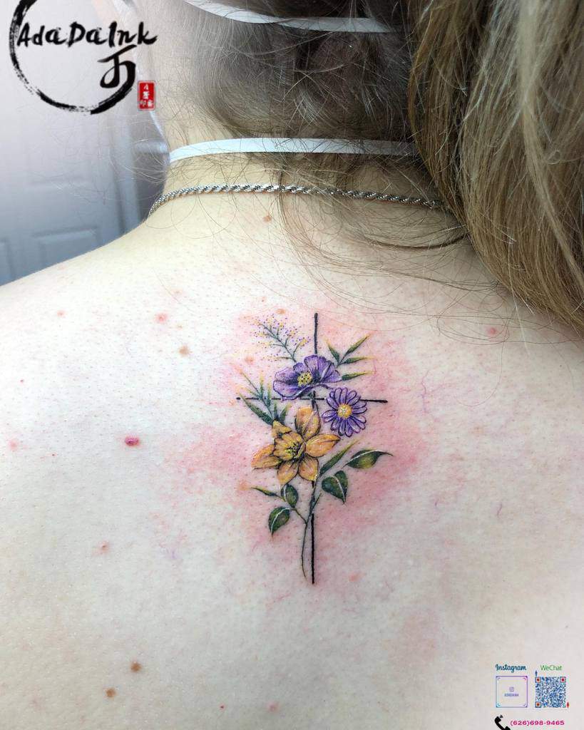 Vibrant floral cross tattoo on the upper back, featuring colorful flowers intertwined with a delicate cross design