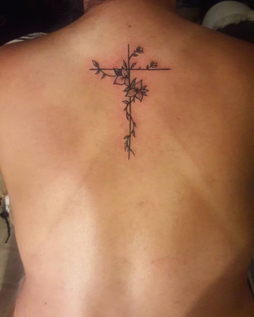 Tattoo of a cross with floral design on an upper back
