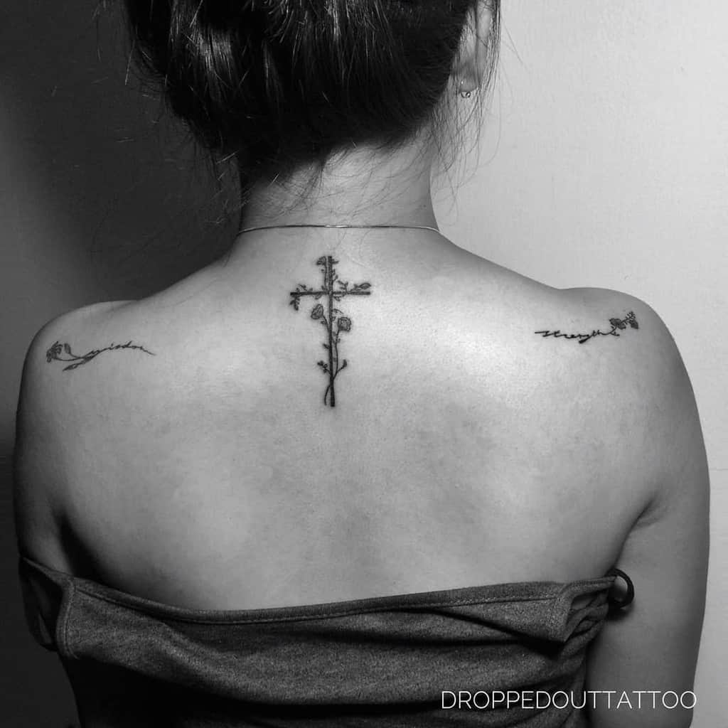 Woman's back with floral cross tattoo in the center and script tattoos on shoulders
