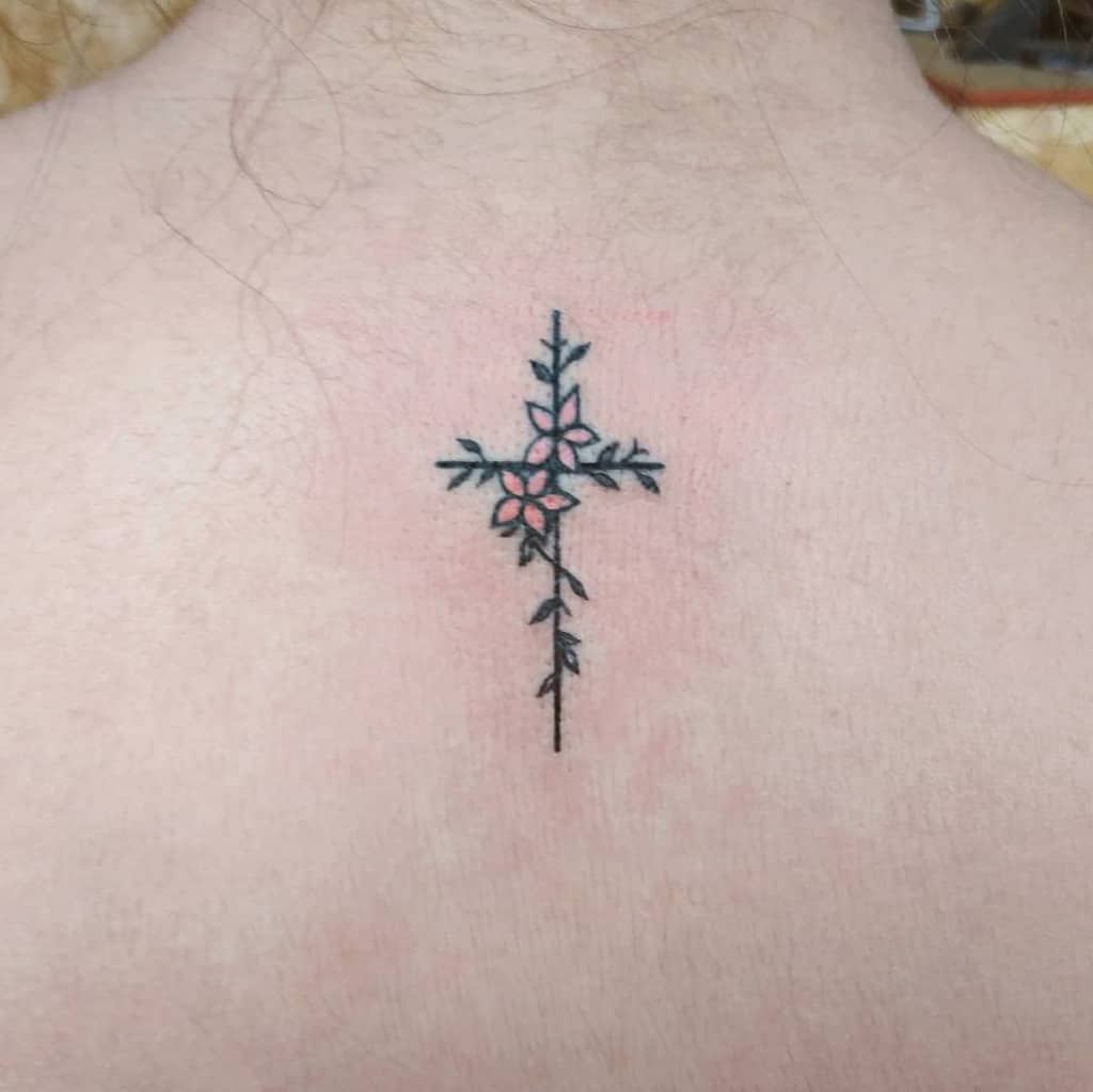 A tattoo of a cross made with vine-like designs and small pink flowers on the back