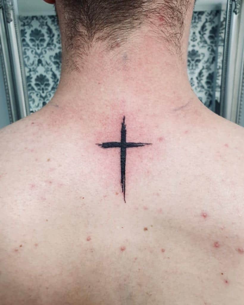 A simple black cross tattoo on the back of a neck