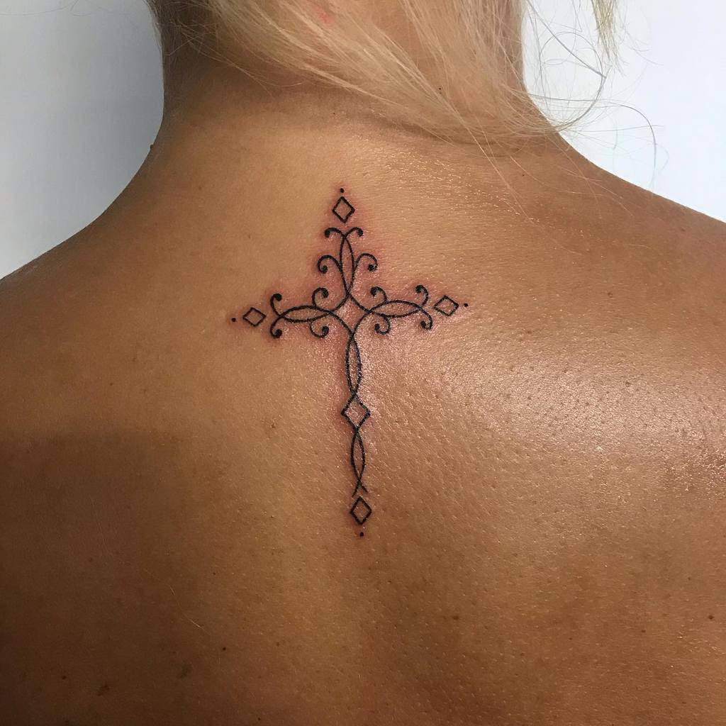 Intricate cross tattoo on upper back with delicate swirls and diamond shapes