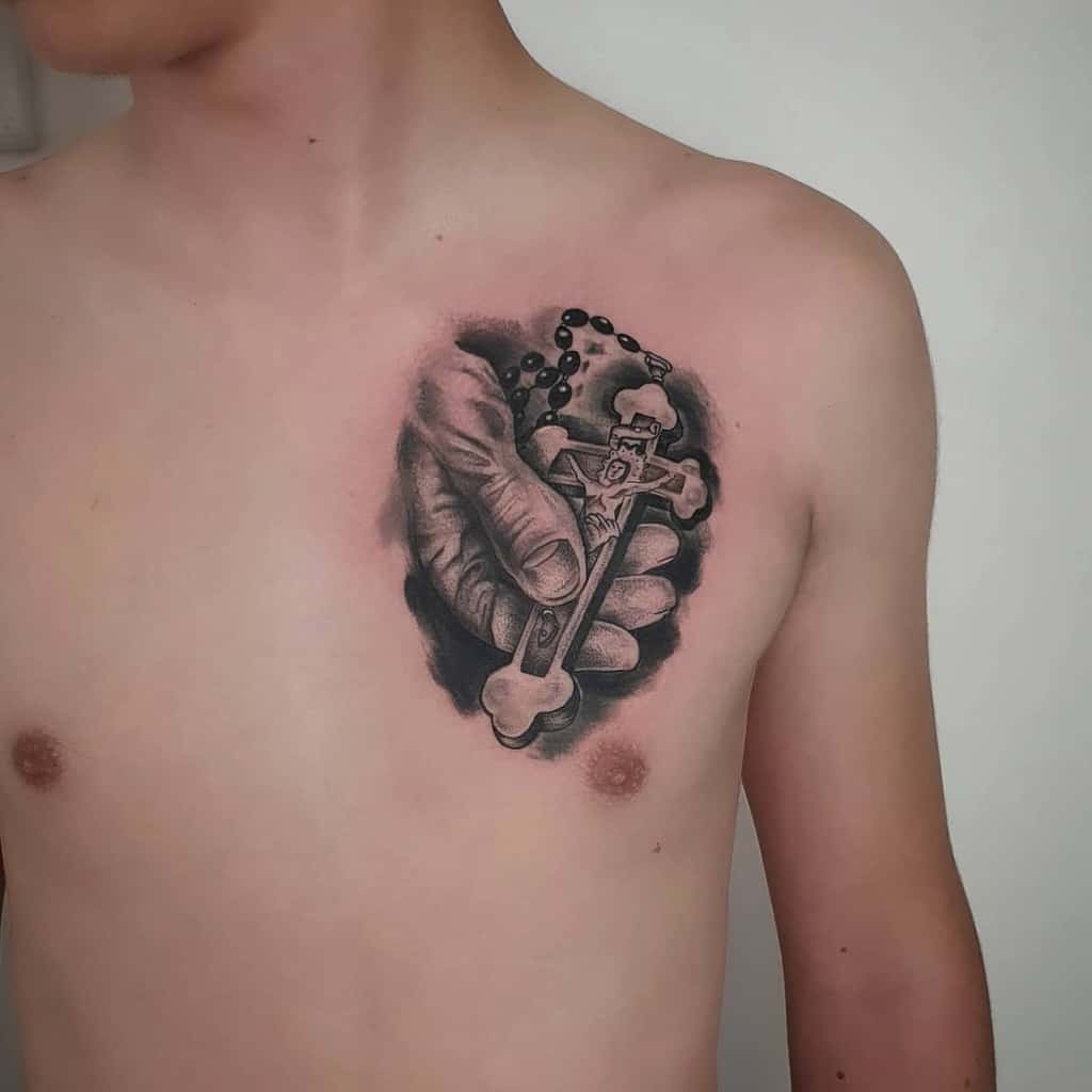 Tattoo on chest of a hand holding a crucifix and rosary