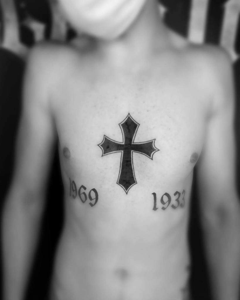 A person with a cross tattoo on their chest and the years "1969" and "1933" on either side