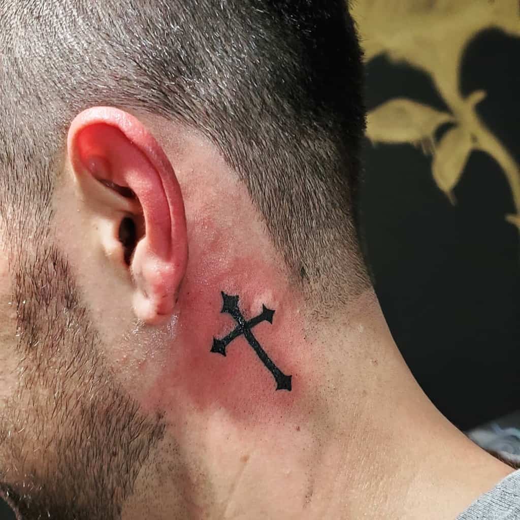Close-up of a man's neck with a black cross tattoo behind his ear