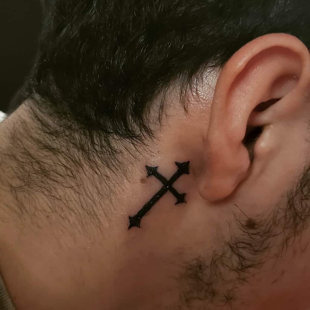 Tattoo of two crossed arrows behind an ear