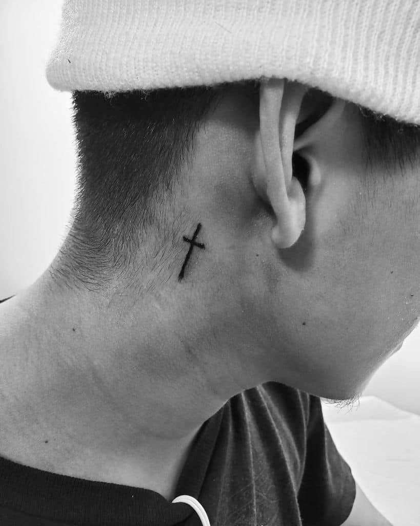 Man's neck with a small cross tattoo behind the ear